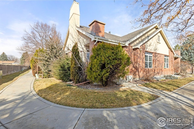 view of side of property with brick siding, a lawn, a chimney, and fence