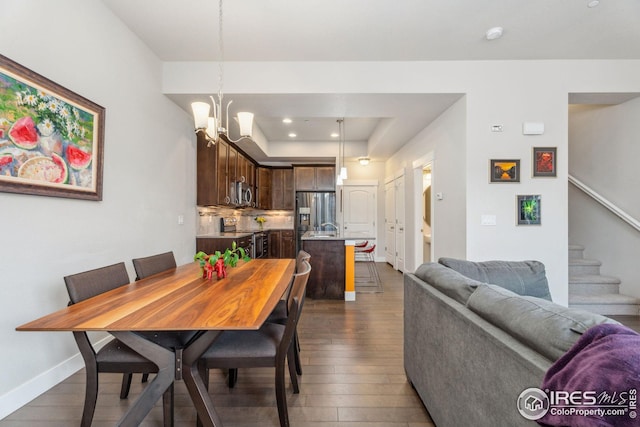 dining space with dark wood-type flooring, a tray ceiling, baseboards, a chandelier, and stairs