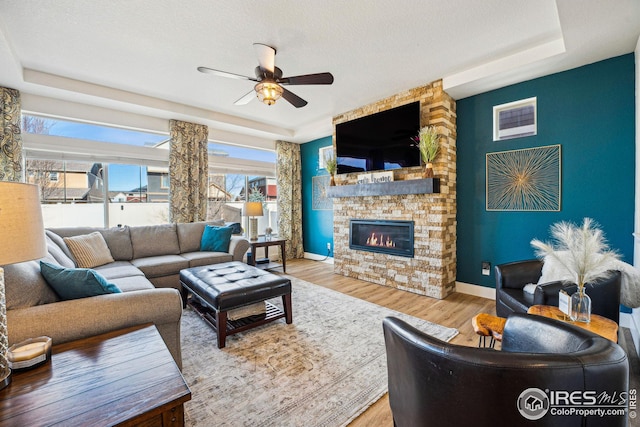 living room with a tray ceiling, baseboards, wood finished floors, and a fireplace