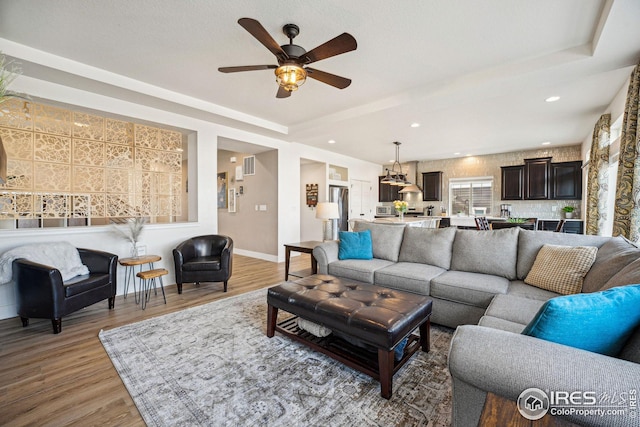 living area with light wood-type flooring, visible vents, a tray ceiling, recessed lighting, and baseboards