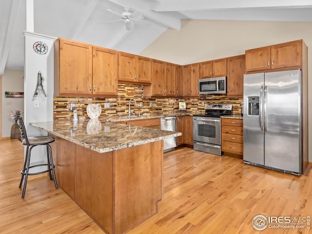 kitchen featuring light stone counters, a peninsula, light wood-style flooring, appliances with stainless steel finishes, and tasteful backsplash