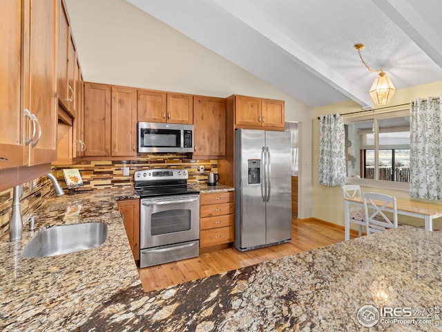 kitchen with brown cabinetry, light stone countertops, lofted ceiling, a sink, and appliances with stainless steel finishes