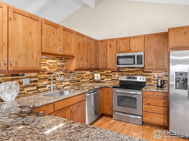 kitchen with a sink, dark stone countertops, backsplash, stainless steel appliances, and light wood-style floors