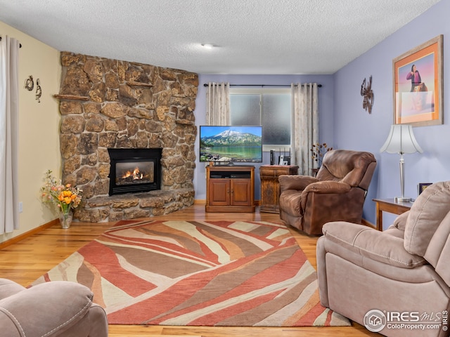 living area with a stone fireplace, a textured ceiling, baseboards, and wood finished floors