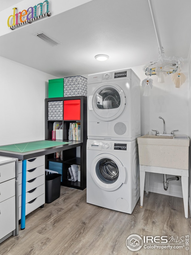 laundry area with visible vents, stacked washer and clothes dryer, laundry area, and wood finished floors