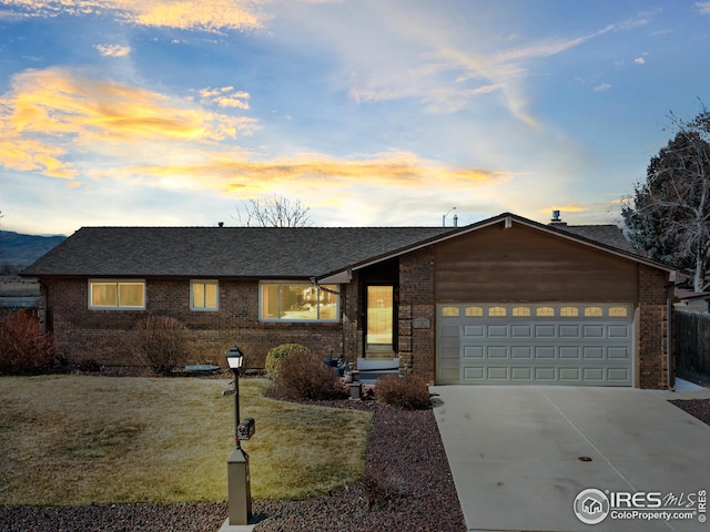 view of front of property featuring brick siding, a yard, driveway, and a garage