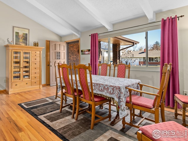 dining space with vaulted ceiling with beams, wood finished floors, and a textured ceiling