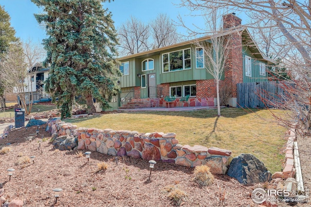 view of front of property with a patio, board and batten siding, a front yard, brick siding, and a chimney