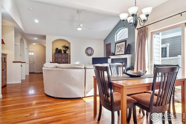 dining area with light wood finished floors, a healthy amount of sunlight, a fireplace, and vaulted ceiling