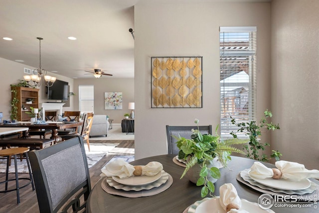 dining space featuring ceiling fan with notable chandelier, visible vents, wood finished floors, and a healthy amount of sunlight