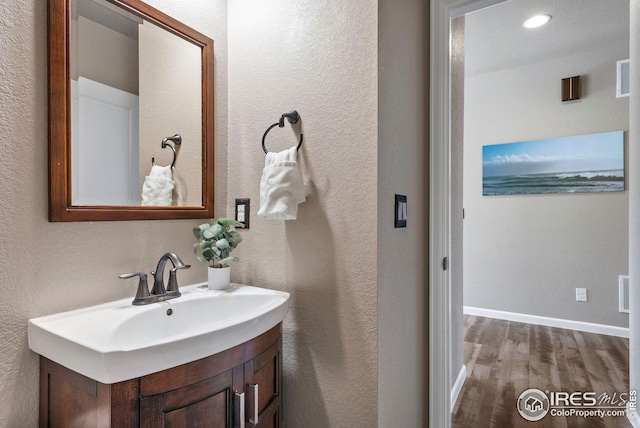 bathroom featuring baseboards, wood finished floors, a textured wall, and vanity