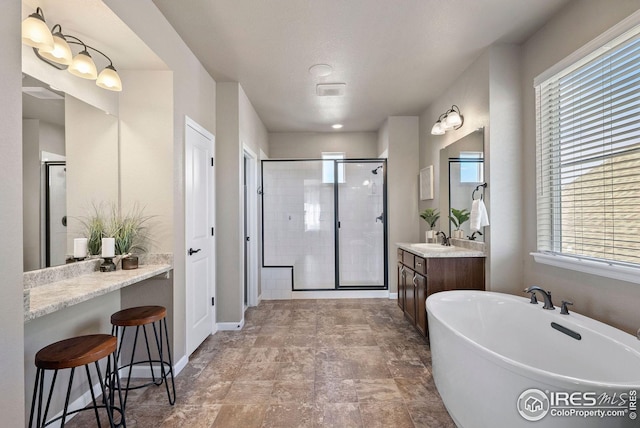 bathroom with stone finish floor, vanity, baseboards, a stall shower, and a soaking tub