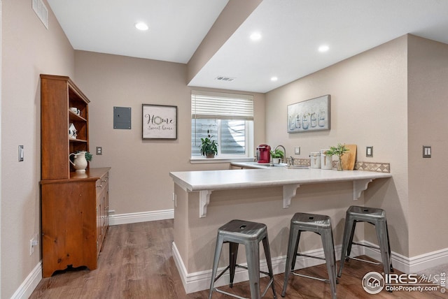 kitchen with wood finished floors, light countertops, a kitchen bar, baseboards, and a peninsula