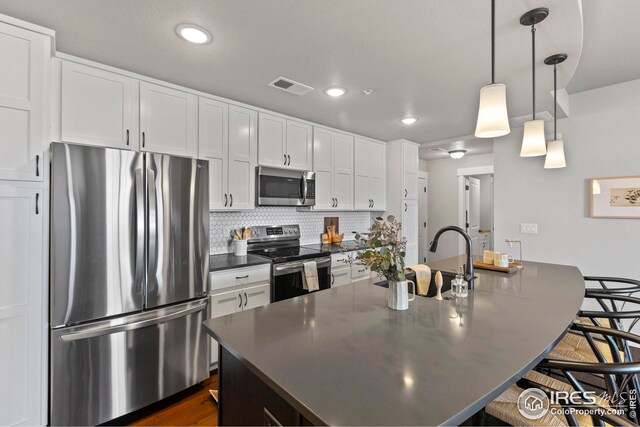 kitchen featuring dark countertops, visible vents, an island with sink, a kitchen breakfast bar, and stainless steel appliances