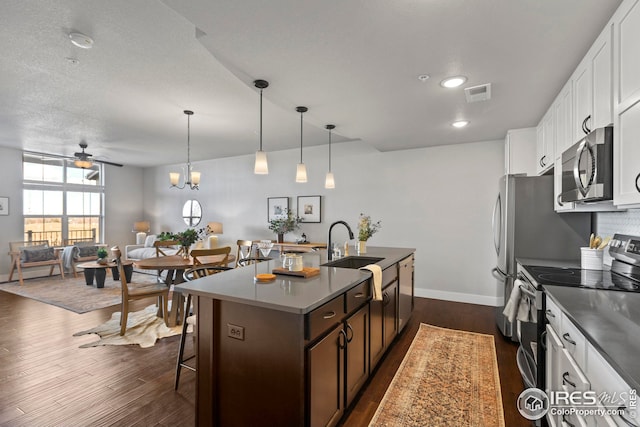 kitchen with dark wood-style floors, a center island with sink, visible vents, a sink, and appliances with stainless steel finishes