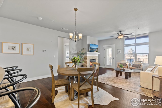 dining area with visible vents, baseboards, ceiling fan with notable chandelier, wood finished floors, and a glass covered fireplace