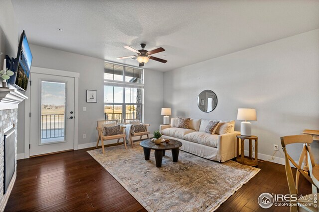 living room featuring baseboards, a textured ceiling, a fireplace, and dark wood-style flooring