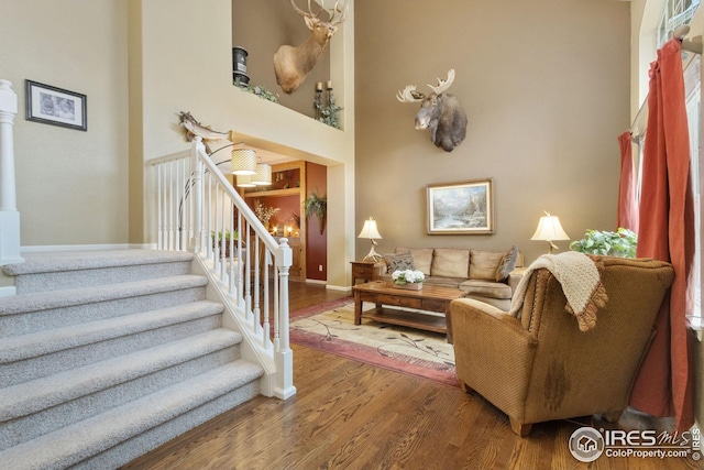 living area with a towering ceiling, baseboards, wood finished floors, and stairs