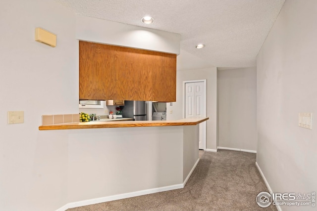 kitchen featuring a textured ceiling, brown cabinets, freestanding refrigerator, baseboards, and carpet floors
