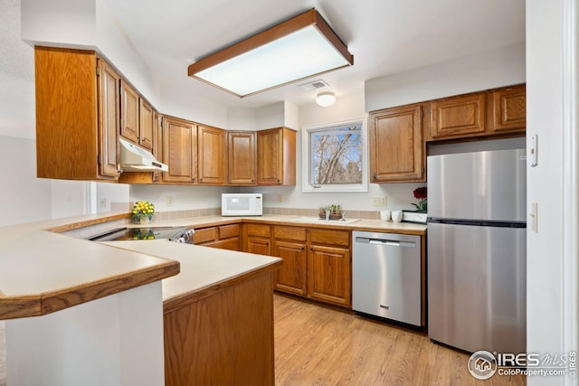 kitchen featuring stainless steel appliances, a peninsula, under cabinet range hood, and brown cabinets
