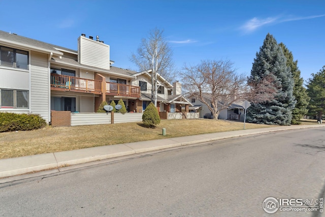 view of front of house with a front lawn, a chimney, a balcony, and brick siding