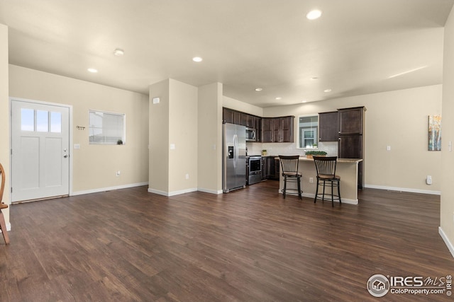 kitchen with dark wood-style flooring, decorative backsplash, dark brown cabinets, appliances with stainless steel finishes, and a kitchen breakfast bar