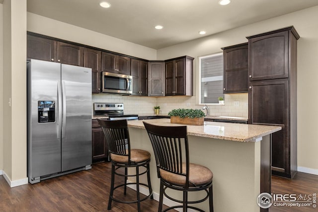 kitchen with a kitchen island, dark wood finished floors, stainless steel appliances, dark brown cabinets, and a kitchen breakfast bar