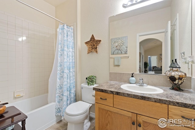 bathroom featuring vanity, toilet, a textured wall, and shower / bath combo
