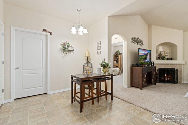 dining area with a chandelier, light colored carpet, lofted ceiling, a lit fireplace, and arched walkways