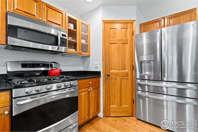 kitchen with brown cabinetry, light wood finished floors, stainless steel appliances, and glass insert cabinets