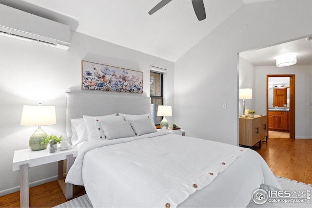 bedroom with baseboards, a wall unit AC, vaulted ceiling, ensuite bathroom, and light wood-style floors