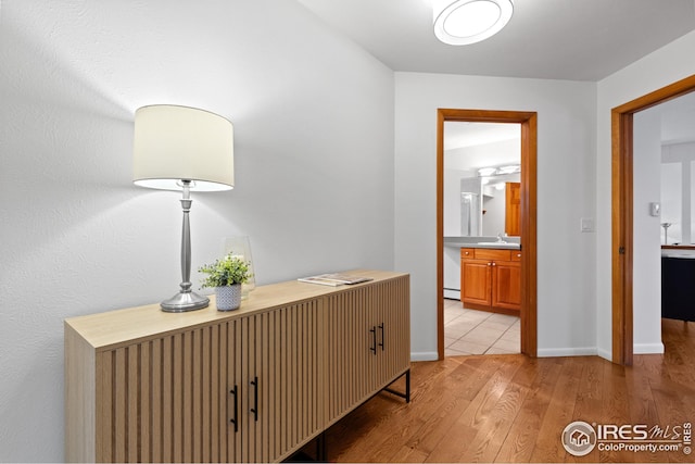 hall with baseboards, light wood finished floors, and a sink