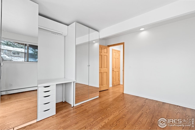 unfurnished bedroom with baseboard heating, recessed lighting, light wood-type flooring, and a wall unit AC