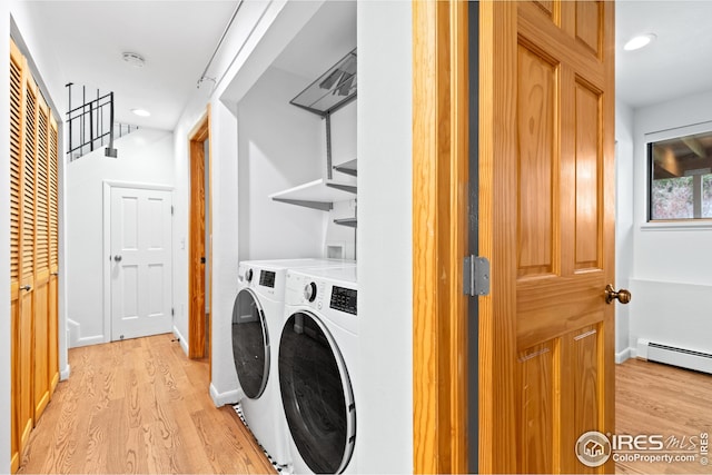 clothes washing area with a baseboard radiator, independent washer and dryer, light wood-style flooring, and laundry area