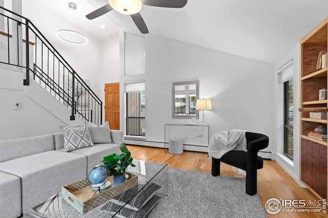 living area with stairs, high vaulted ceiling, wood finished floors, and a baseboard radiator