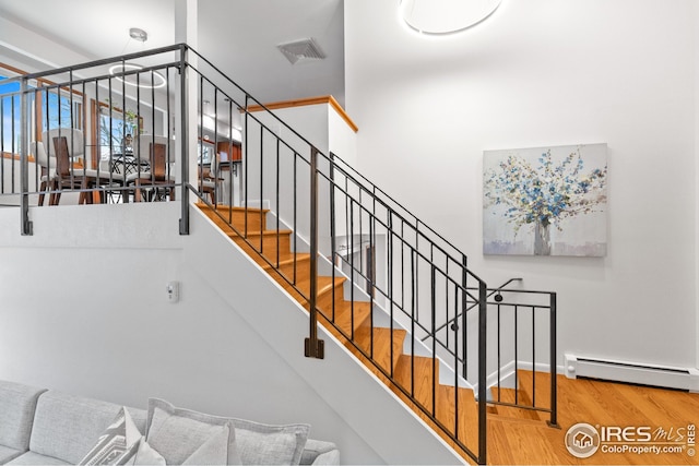 stairs featuring visible vents, baseboard heating, and wood finished floors