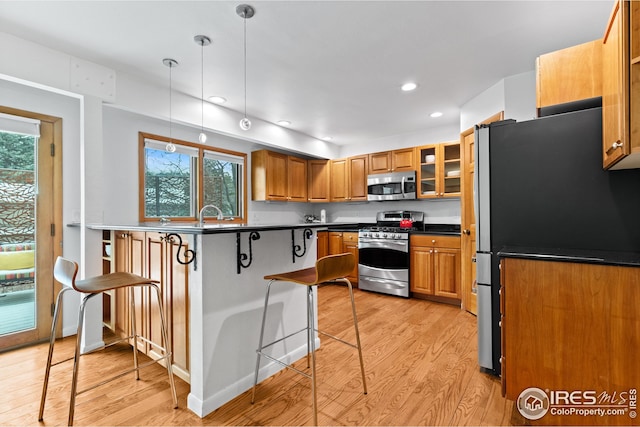 kitchen with brown cabinetry, light wood-style flooring, plenty of natural light, appliances with stainless steel finishes, and a kitchen bar