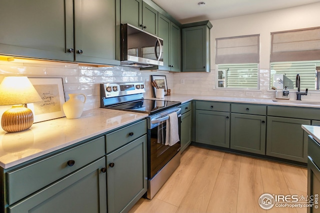 kitchen featuring light wood finished floors, a sink, stainless steel appliances, green cabinets, and tasteful backsplash