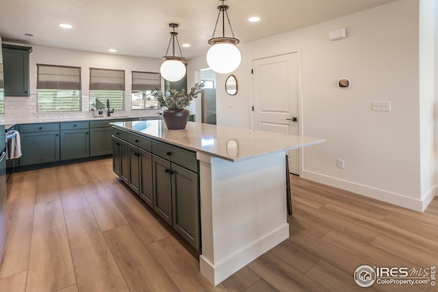 kitchen featuring pendant lighting, light wood-style flooring, tasteful backsplash, a center island, and light stone countertops