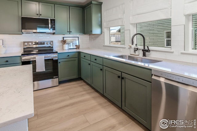 kitchen featuring a sink, appliances with stainless steel finishes, decorative backsplash, and green cabinetry