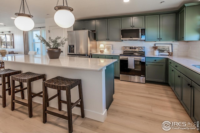 kitchen featuring a breakfast bar area, light stone counters, light wood-style flooring, stainless steel appliances, and tasteful backsplash