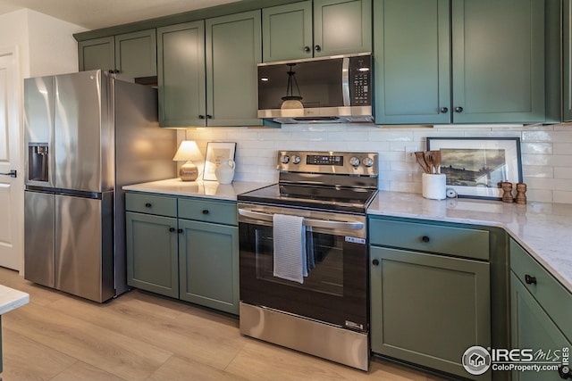 kitchen with backsplash, stainless steel appliances, green cabinets, light wood finished floors, and light stone countertops