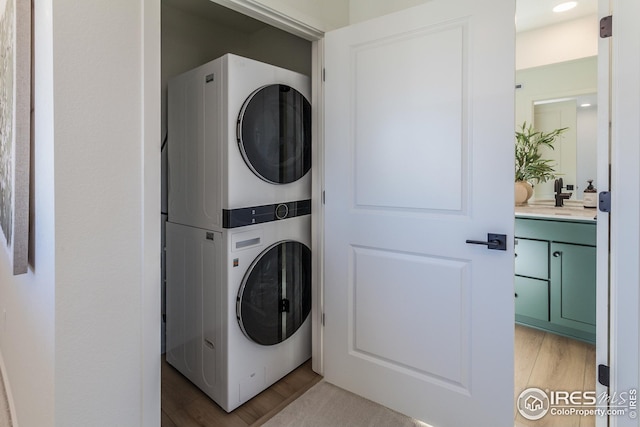 laundry area featuring a sink, light wood-style floors, stacked washer and clothes dryer, and laundry area