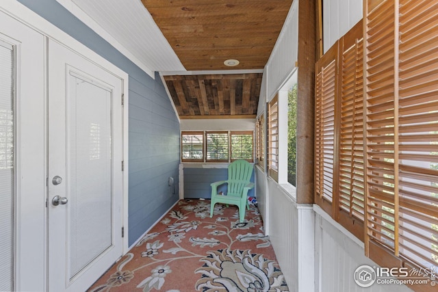 hall with lofted ceiling, wooden walls, and wood ceiling