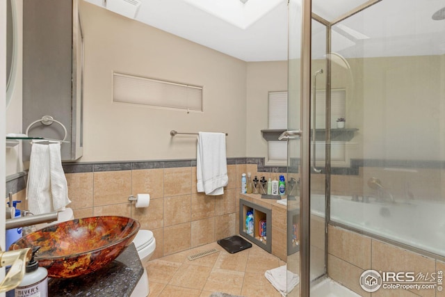 full bath featuring visible vents, toilet, a sink, a tile shower, and a skylight