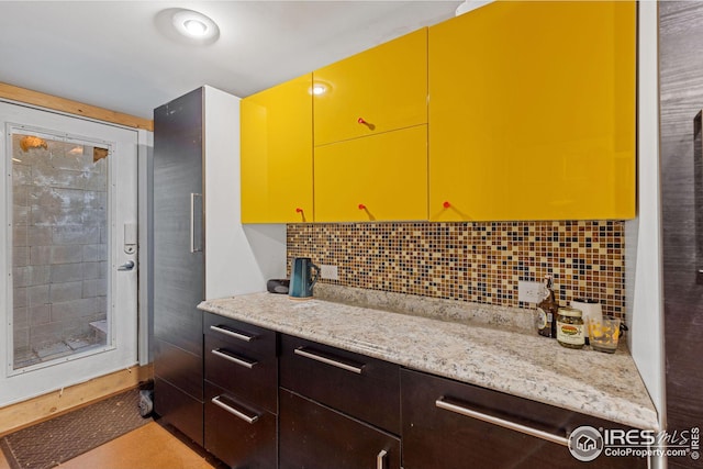 kitchen featuring dark brown cabinetry, light stone counters, and tasteful backsplash