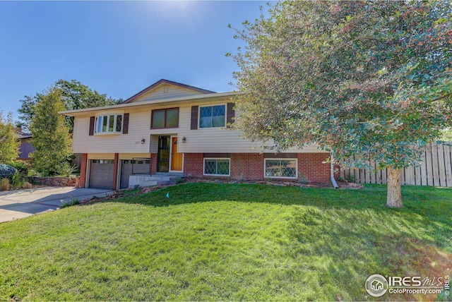 bi-level home featuring driveway, fence, a front yard, an attached garage, and brick siding