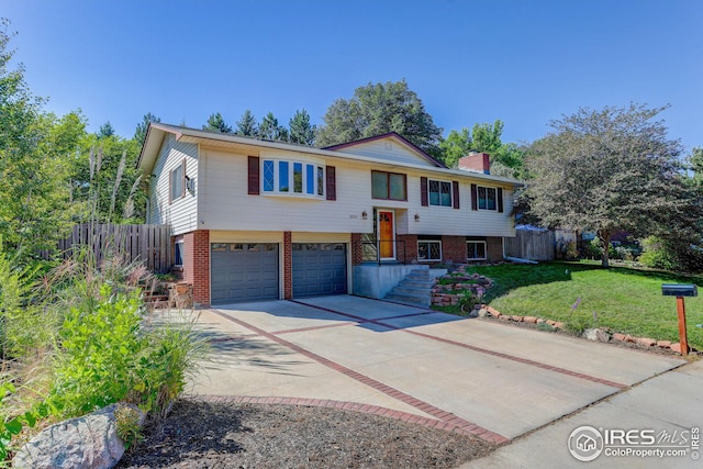 raised ranch featuring brick siding, concrete driveway, a front lawn, and fence