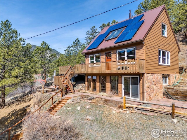 back of house featuring solar panels, a deck with mountain view, stone siding, and stairway