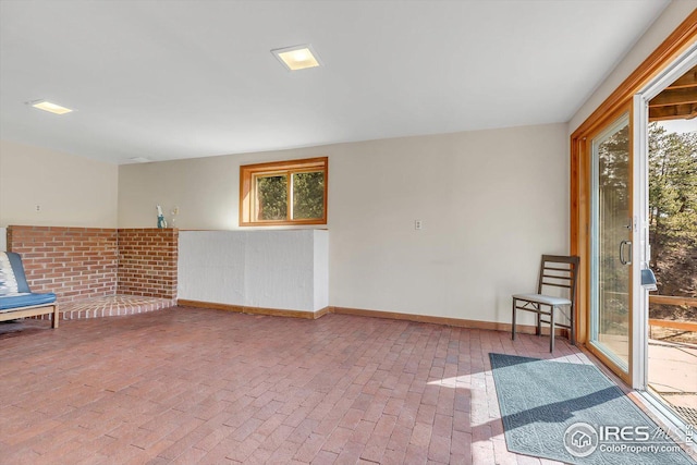 unfurnished room featuring brick floor and baseboards